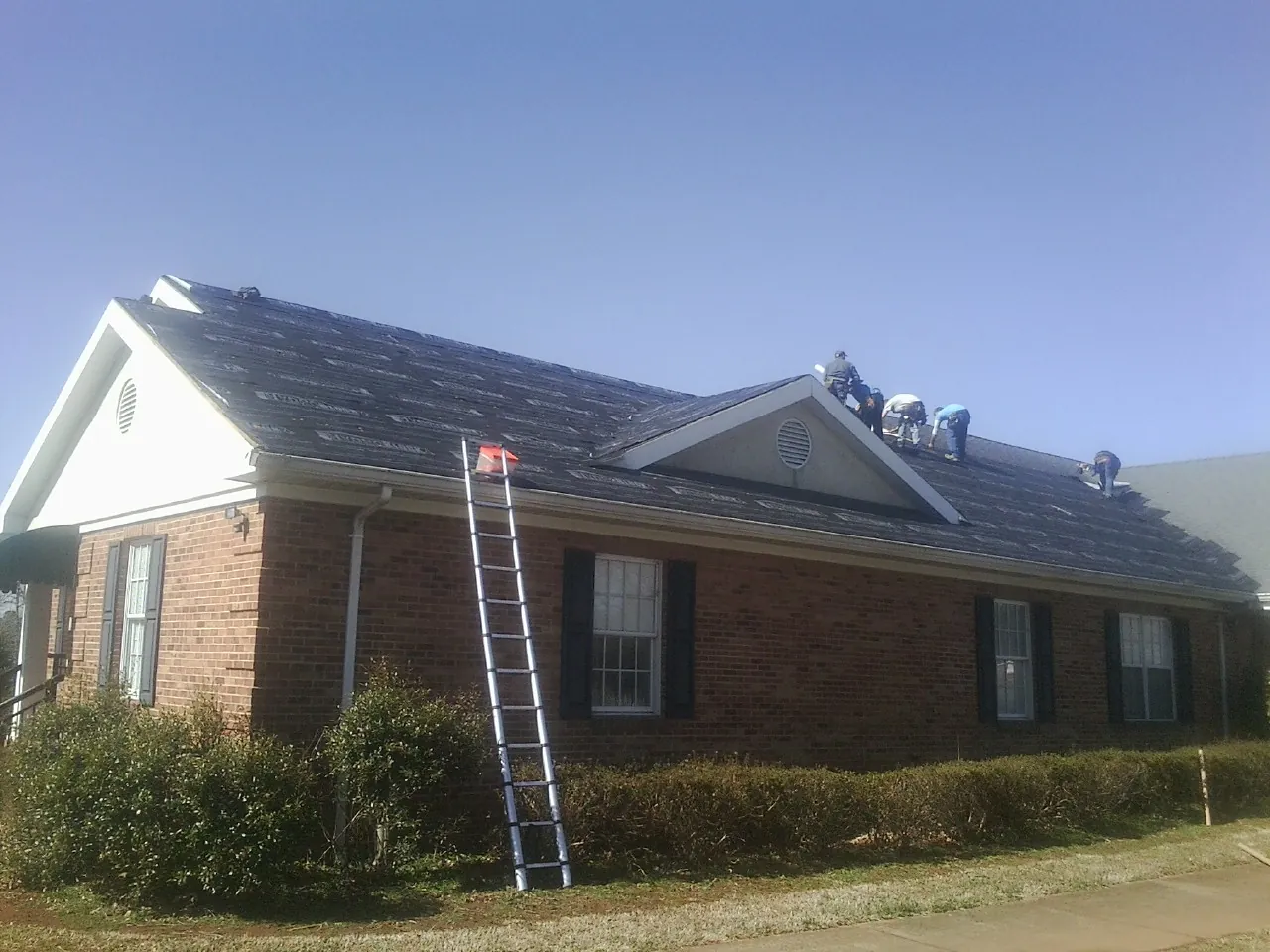 Crew tearing shingles off a brick ranch roof with a ladder set — Emergency Roof Repair work by our crew in Foster