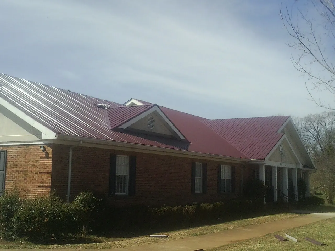 Red metal roof with gabled entries on a long brick building, from a Hail Damage Roof Repair job in Foster