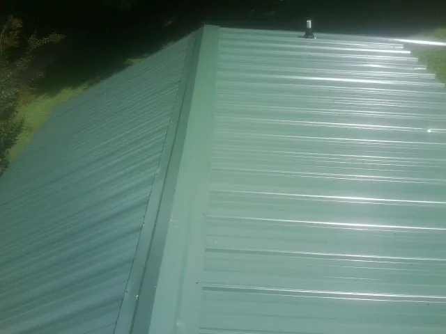 New green metal panels meeting at the ridge of a roof — Flat Roof Repair work by our crew in Foster