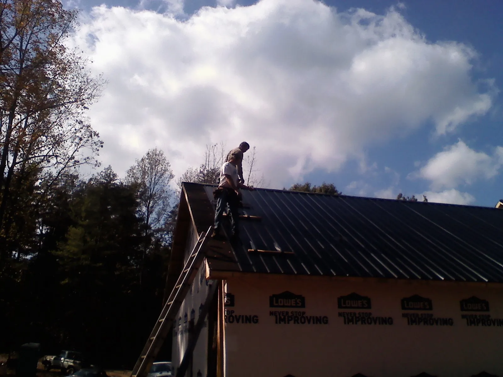 Roofer fastening dark metal panels high against a cloudy sky, from a Roof Inspection job in Foster
