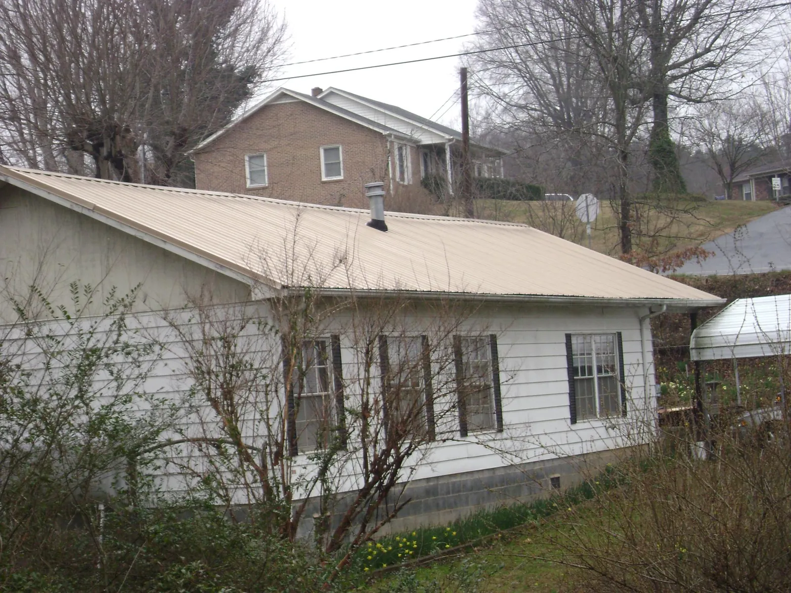 Tan metal roof on a white sided house set into a hillside — Commercial Roofing by Roofing Brothers in Foster